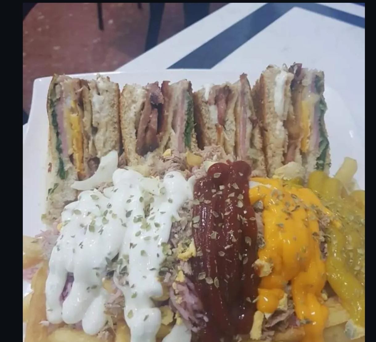 Sándwich Club Dany Melo cortado en cuartos, con papas y tres salsas